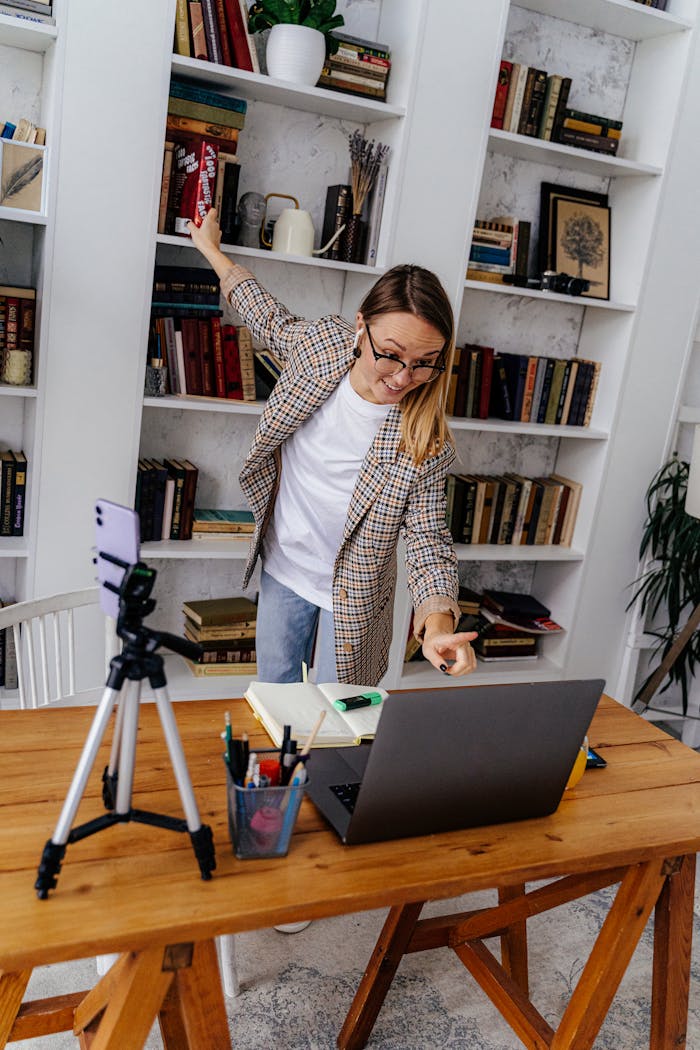 Woman teaching online with a laptop and smartphone in a home library setting.
