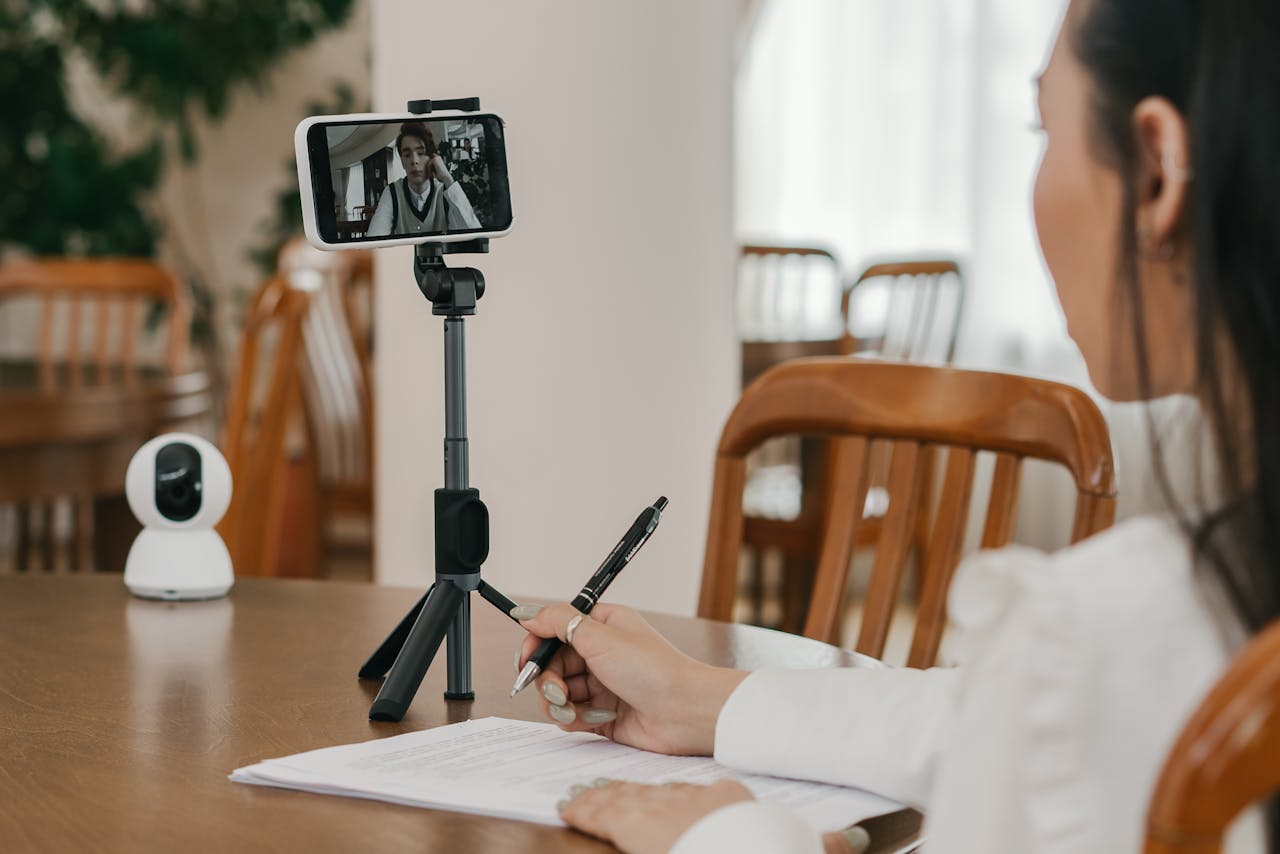 A woman taking notes during an online class with a smartphone on a tripod.